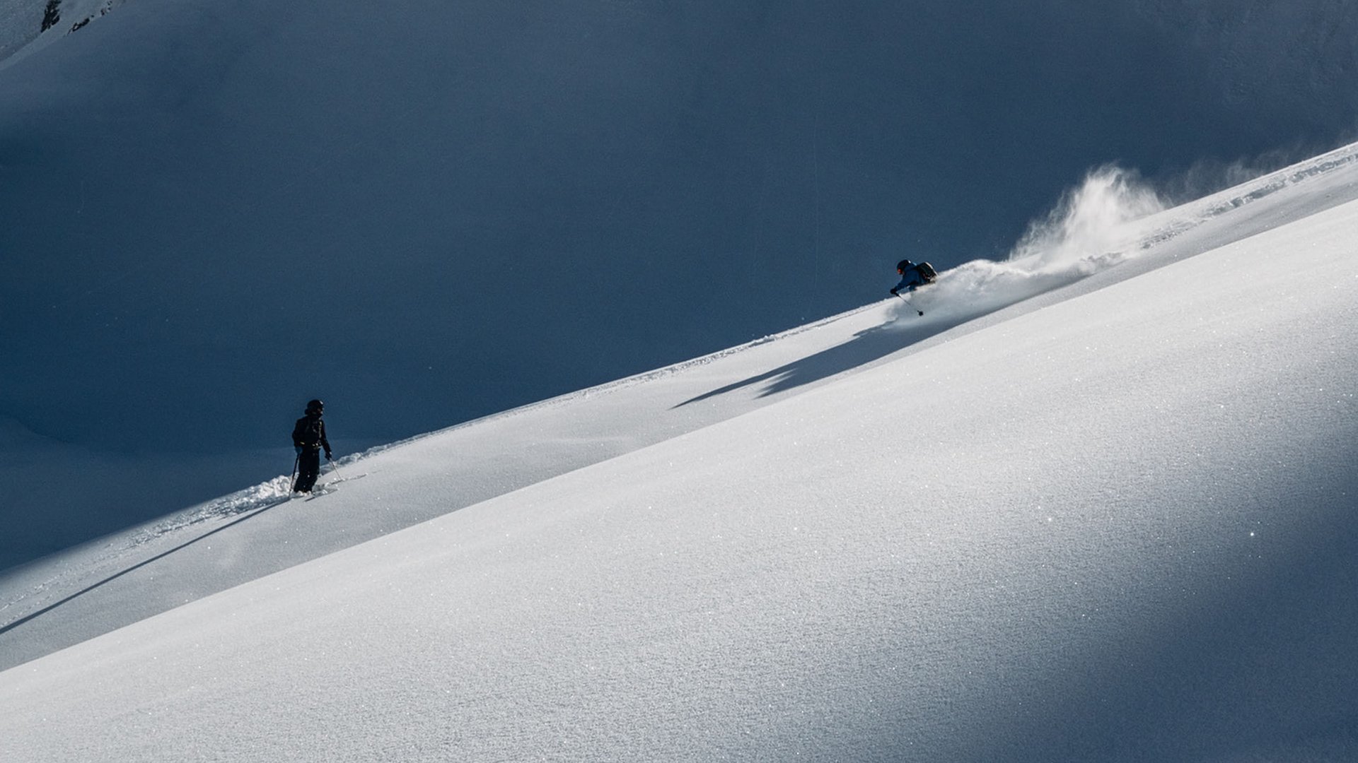 Ski Arlberg: Unterkunft gesucht? Haus Braunarl! Zwei Skifahrer auf verschneitem Berghang, einer fährt, einer steht still